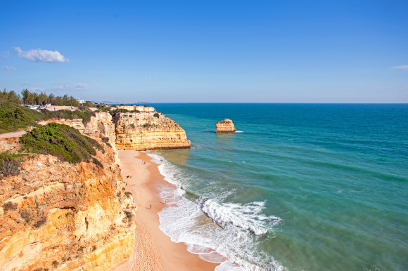 A view of the striking cliffs at Praia da Marinha Beach in Portugal surrounded by golden sand and azure waters